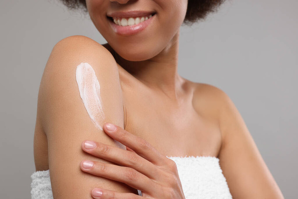 Young woman applying body cream onto shoulder on grey background, closeup - Foto, afbeelding