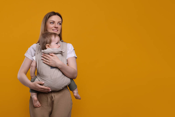 Mother holding her child in sling (baby carrier) on orange background - Φωτογραφία, εικόνα