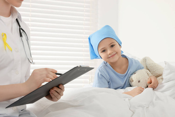 Cáncer infantil. Doctor con portapapeles y pequeño paciente con conejito de juguete en el hospital - Foto, Imagen