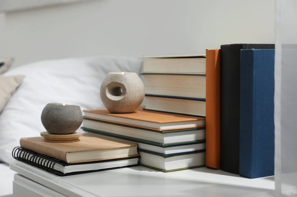 Hardcover books and scented candles on white bedside table indoors - Фото, изображение
