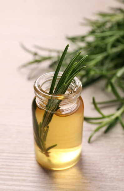 Bottle of essential oil and fresh rosemary on white wooden table, closeup - 写真・画像