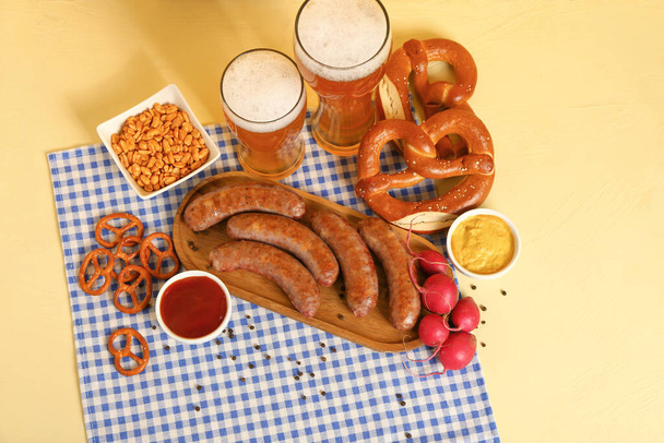 Gläser mit kaltem Bier und verschiedene Snacks auf gelbem Hintergrund. Oktoberfest-Feier - Foto, Bild