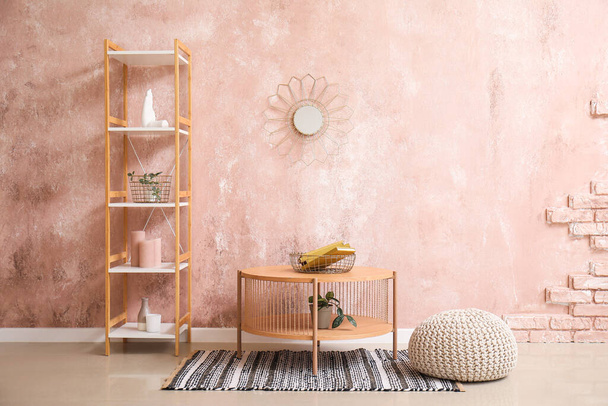 Дерев'яний журнальний столик, пуф і стелаж біля гранжевої рожевої стіни - Фото, зображення