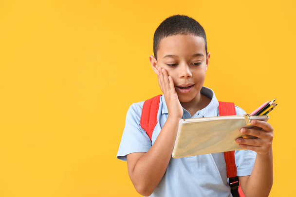 Meglepett kis afro-amerikai iskolás fiú tolltartó narancssárga háttér - Fotó, kép