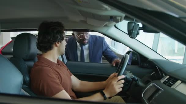 Młody człowiek z Bliskiego Wschodu wybiera nowy samochód w centrum dealerskim zadając pytania o deskę rozdzielczą sprzedawcy Afroamerykanów - Materiał filmowy, wideo
