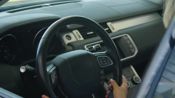 Lähikuva onnellinen nuori valkoihoinen nainen, joka valitsee uuden auton jälleenmyyntikeskuksessa nauttien koskettavasta ohjauspyörästä ja kojelaudasta - Materiaali, video