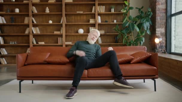 Alegre chico albino hipster tocando guitarra invisible divertirse en el sofá en apartamento de estilo loft moderno. Entretenimiento moderno, música y concepto de jóvenes felices. extático macho profundo en su sueños 4K - Metraje, vídeo