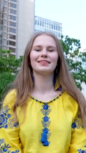 χαριτωμένο όμορφη ξανθιά κοπέλα νεαρή γυναίκα κοιτάζει στο πλαίσιο και κάνει μια καρδιά με τα χέρια. χαρούμενη σε ένα κίτρινο πουκάμισο σε ένα λευκό-πράσινο φόντο δρόμο αγάπη ειρήνη στην Ουκρανία ηρεμία χαρά - Πλάνα, βίντεο