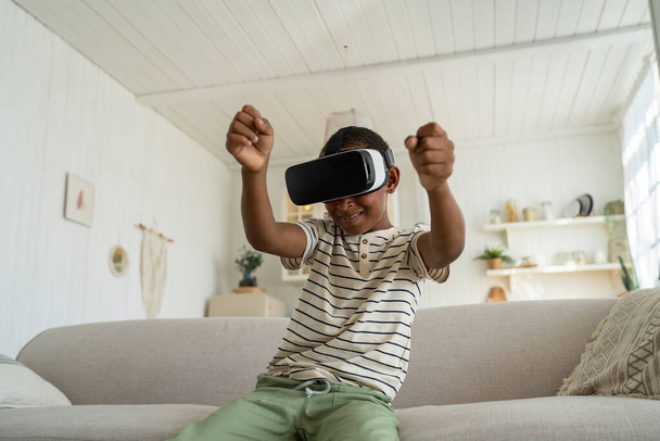Odaklanmış Afrikalı Amerikalı çocuk sanal gerçeklik kulaklığıyla araba sürüyor. Siber uzayda hareket eden meraklı gençler evdeki kanepede oturuyor. Boş zaman, eğlence konsepti. - Fotoğraf, Görsel