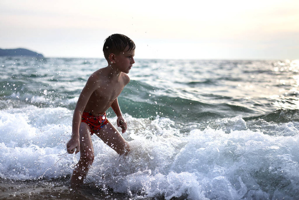 Boy Surfer na praia com ondas com muitos respingos. Estilo de vida familiar ativo, crianças esportes aquáticos ao ar livre, aulas de natação no acampamento de surf. Férias de verão com uma criança. - Foto, Imagem