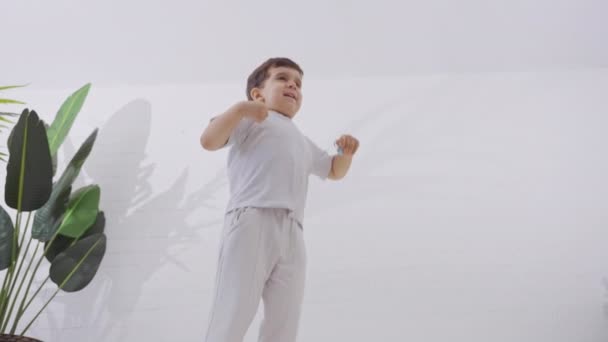 Actieve blanke jongen die op bed springt. Vrolijk kind stuitert op wit beddengoed in de ochtend. Concept van geluk en vrijheid. Langzame beweging.  - Video
