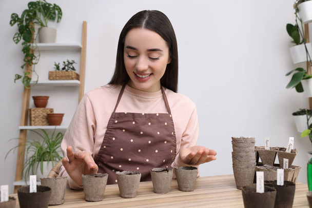 Woman planting vegetable seeds into peat pots with soil at wooden table indoors - Foto, Imagen