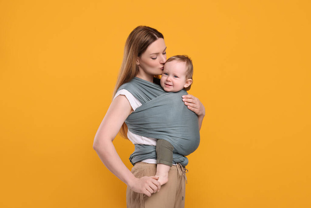 Mother holding her child in baby wrap on orange background - Фото, зображення