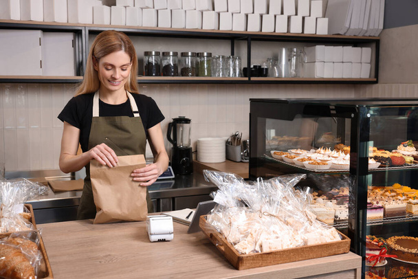 Happy seller with paper bag at cashier desk in bakery shop - Foto, Imagem