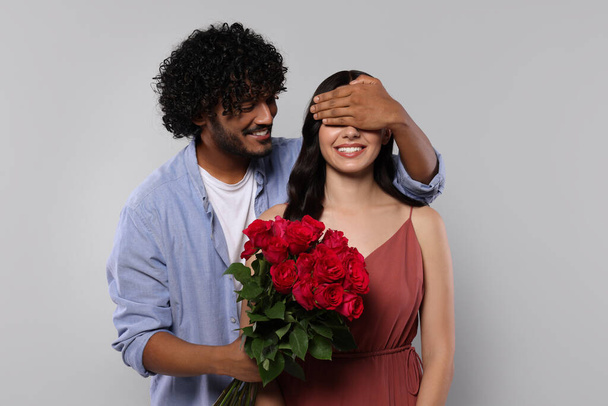 International dating. Handsome man presenting roses to his beloved woman on light grey background - Foto, Bild