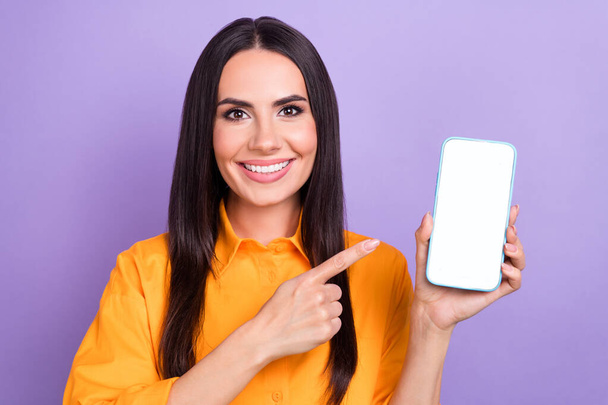 Portrait of positive girlish woman long hairstyle wear oversize shirt indicating at smartphone screen isolated on violet color background. - Foto, immagini