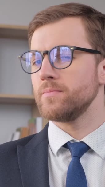 Portrait of an office worker wearing glasses, he is looking at the camera and smiling. Work of a manager in the office. Businessmen. Vertical video - Кадры, видео