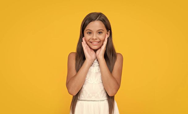 smiling teen girl in white dress has long hair on yellow background. - Photo, Image