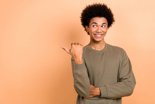 Portrait of cheerful young person afro hairdo dressed khaki shirt look at sale indicating empty space isolated on beige color background. - Foto, afbeelding