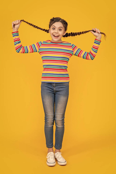 photo of amazed teen braided girl. childhood studio shot of teen braided girl. teen braided girl isolated on yellow background. teen girl with braided hair in studio. - 写真・画像