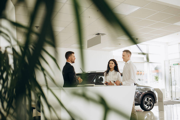 Middle age couple choosing and buying car at car showroom. Car salesman gives them car keys - Fotó, kép