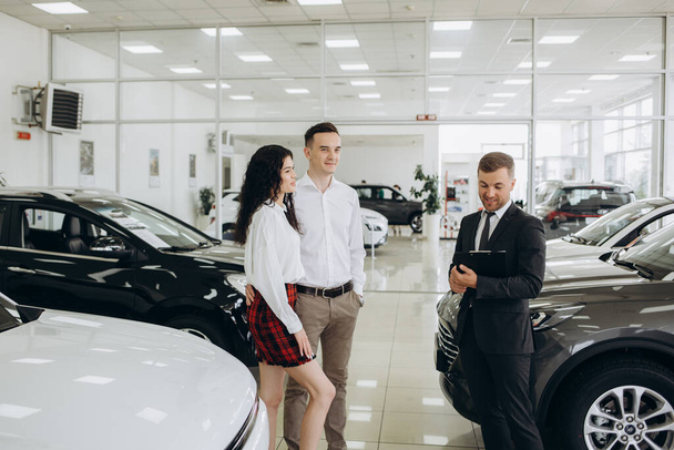 Car dealer showing car to couple in showroom. - Foto, Bild