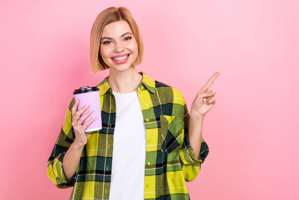 Photo portrait of attractive young woman finger point empty space paper cup wear plaid yellow clothes isolated on pink color background. - Fotoğraf, Görsel