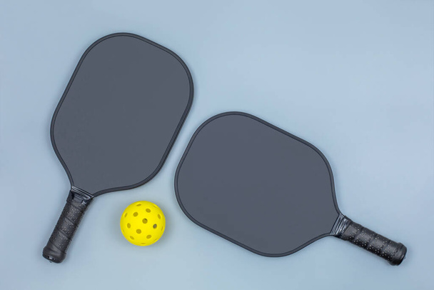 Closeup top view of two black pickleball paddles and a yellow ball on light gray background with copy space - Photo, Image