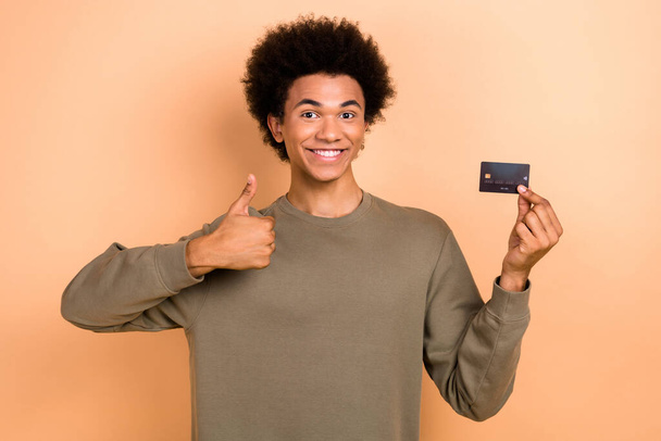 Portrait of nice handsome person afro hairdo dressed khaki pullover hold plastic card show thumb up isolated on beige color background. - Фото, зображення