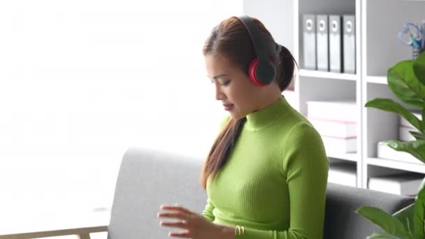 Houkutteleva aasialainen nainen lepää mukava olohuone ja kannettavan tietokoneen ja kuunnella musiikkia, rentoutua, sohva, elämäntapa. Laadukas 4k kuvamateriaalia - Materiaali, video