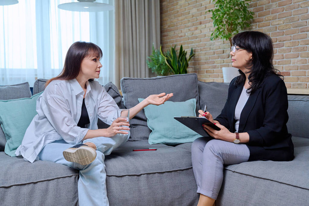 Middle-aged woman at meeting with psychologist counselor, sitting on couch in office. Mental problems of age female, psychological support help. Psychology psychotherapy therapy treatment healthcare - Foto, Imagen