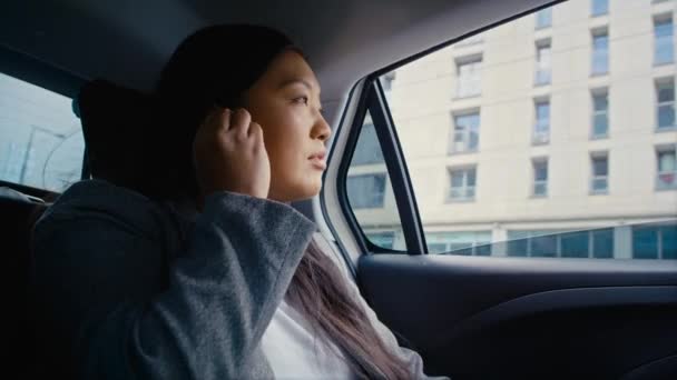 Mujer china de negocios conduciendo en un taxi y usando auriculares. Fotografía con cámara de helio RED en 8K.  - Imágenes, Vídeo