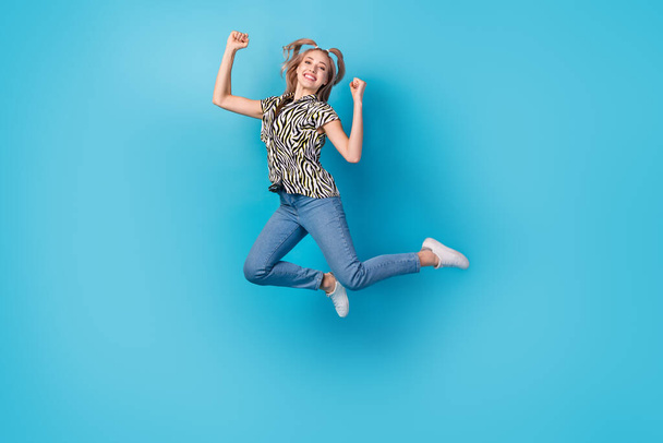 Full size photo of pleasant ecstatic woman dressed zebra shirt jeans white sneakers jumping win betting isolated on blue color background. - Foto, Imagen