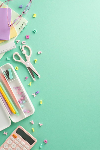 Trendy school supplies setup. Vertical top view of girlish notebooks, pencil case, pens, pins, clips, scissors, calculator, letters on appealing teal background. Space for text or advert integration - Photo, Image