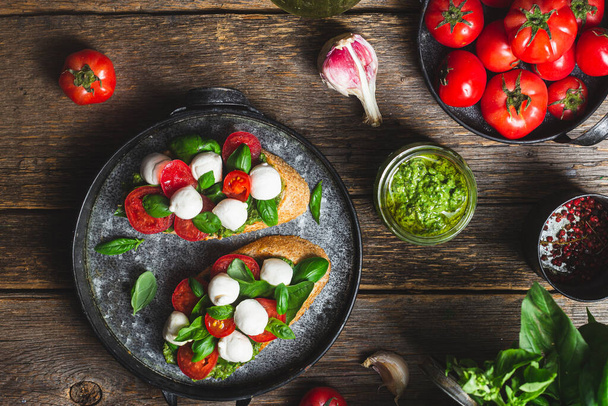  Bruschetta com mussarela, tomates, manjericão e pesto em uma chapa. Bruschetta Caprese - Foto, Imagem