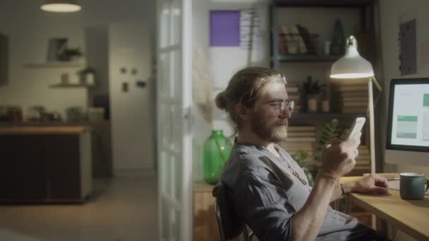 Mittlere Aufnahme eines männlichen Designers, der zu Hause am mit Kerzen dekorierten Arbeitsplatz sitzt, Telefon benutzt und Anruf entgegennimmt - Filmmaterial, Video