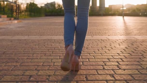 Gün batımında, kot pantolonlu, şehir parkında yürüyen ince bir kadının arka görünüşü. Sokakta yürüyen güzel figürlü bir kadın. Günbatımında Baştan Çıkarıcı Kız Yürüyüşü. Yavaş Hareket - Video, Çekim