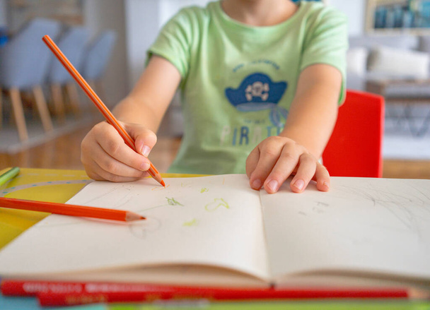 Κοντινό πλάνο των χεριών ενός μικρού παιδιού που ζωγραφίζει με χρωματιστά μολύβια - Φωτογραφία, εικόνα