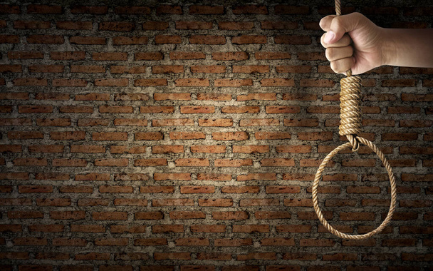 Hand holding rope noose with hangman's knot hanging on dark brick wall - Photo, Image