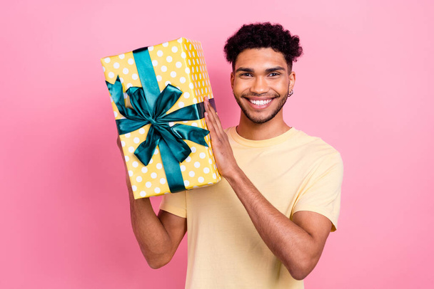Photo of satisfied pleasant friendly guy with earrings dressed stylish yellow t-shirt hold present box isolated on pink color background. - Photo, image