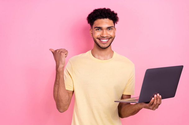 Photo of clever cheerful positive guy dressed yellow stylish t-shirt hold laptop indicating empty space isolated on pink color background. - 写真・画像
