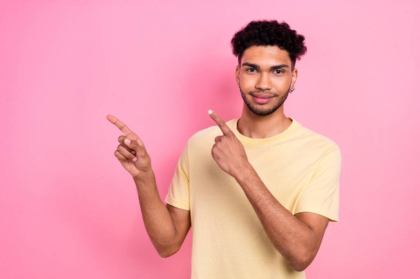 Portrait of cheerful pleasant man with afro hair earrings stubble indicating at offer empty space isolated on pink color background. - Valokuva, kuva