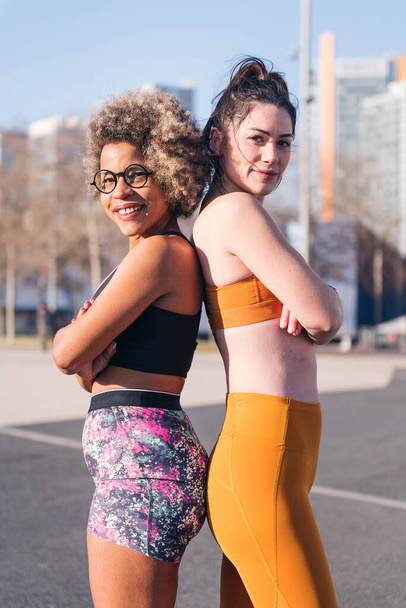 vertical portrait of two female runners standing looking at camera with arms crossed in the city, concept of friendship and sportive lifestyle - Foto, afbeelding