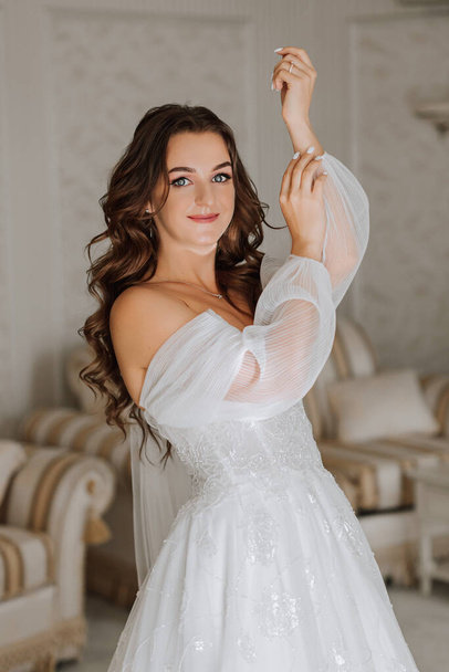 fragile and elegant bride with long brown hair in wedding dress posing for photographer. The girl looks into the lens - Foto, afbeelding
