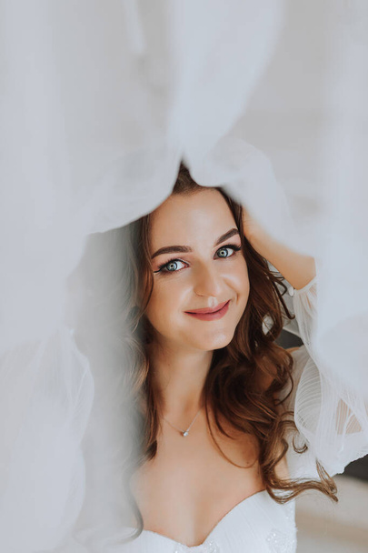 beautiful and gentle girl bride with long brown hair under a veil looks into the camera lens - Photo, Image