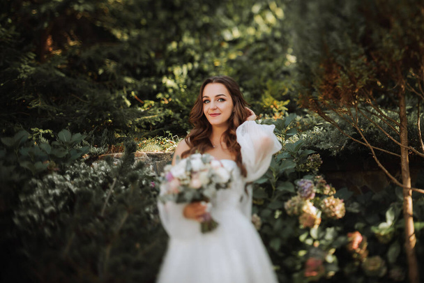 young and beautiful bride with long brown hair in a wedding dress outdoors with a wedding bouquet of flowers. Portrait on the TS-E lens - Photo, Image
