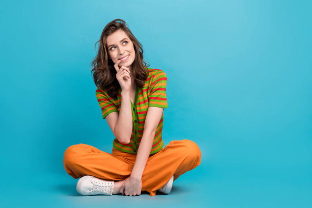 Full length photo of nice thoughtful girl wear striped shirt orange trousers look at promo empty space isolated on blue color background. - Photo, image