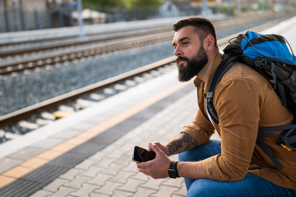 Homem adulto está sentado na estação ferroviária e esperando a chegada do trem. - Foto, Imagem
