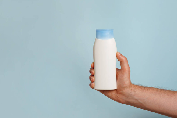 Макет нефирменного белого шампуня или бутылки с кондиционером для брендинга и этикетки и мужской руки на синем фоне. копировальное пространство - Фото, изображение