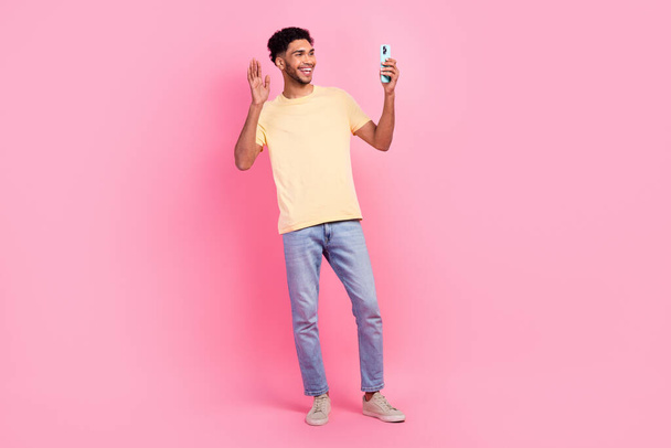 Full size photo of pleasant nice funny man wear yellow t-shirt talk on smartphone video call say hi isolated on pink color background. - Photo, image